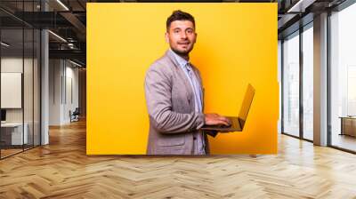 Young handsome man with laptop on yellow background Wall mural